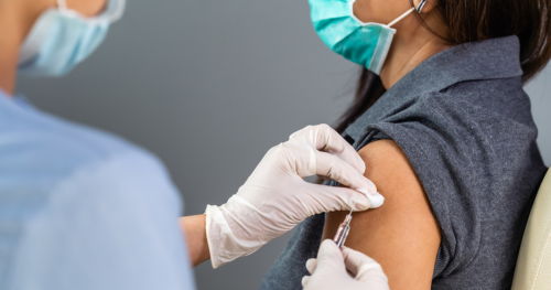 masked doctor gives a masked patient a vaccine with a needle