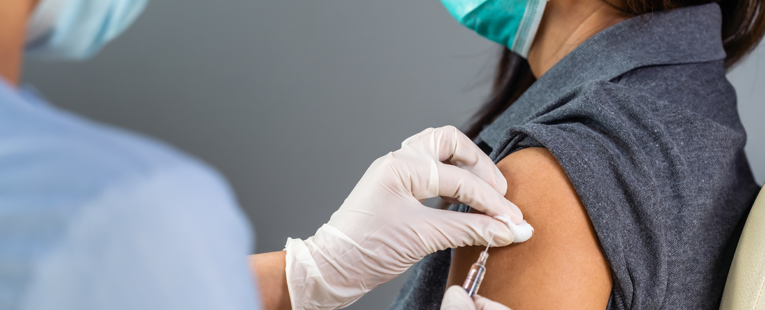 masked doctor gives a masked patient a vaccine with a needle
