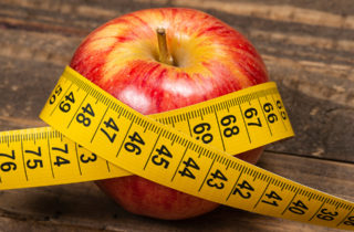 Red apple on table with yellow measuring tape wrapped around it