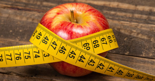 Red apple on table with yellow measuring tape wrapped around it