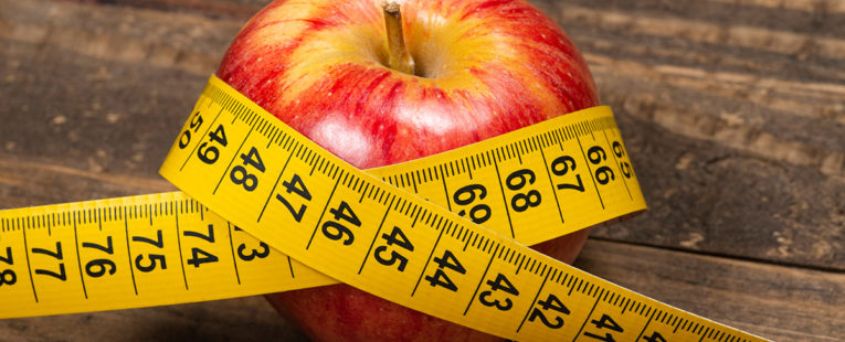 Red apple on table with yellow measuring tape wrapped around it