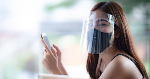 girl wearing a mask and a faceshield reads her cellphone