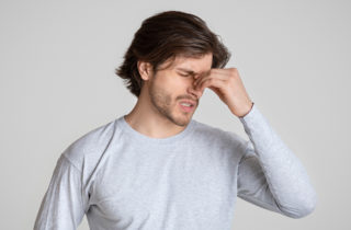 man holds the bridge of his nose in obvious pain