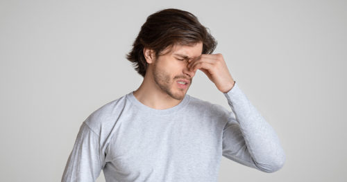 man holds the bridge of his nose in obvious pain