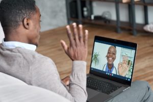 man waves at this laptop where a female doctor waves back through a virtual office visit