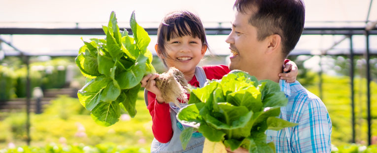 father holds his daughter and both are holding freshly picked vegetables