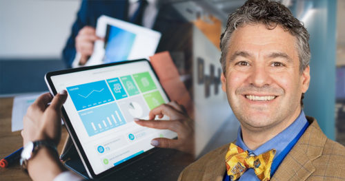Formally dressed faceless woman using tablet computer exploring charts while sitting at table in office during business meeting with colleagues
