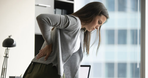 Woman standing at desk holding lower back as if in pain