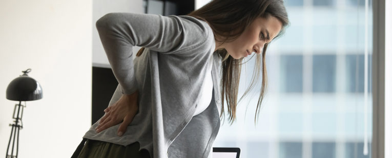 Woman standing at desk holding lower back as if in pain