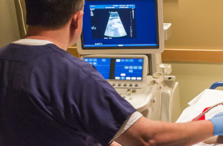 Technician performing ultrasound on senior woman patient with abdominal aortic aneurysm.