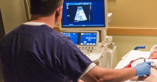 Technician performing ultrasound on senior woman patient with abdominal aortic aneurysm.
