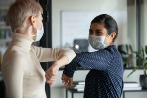Two women touching elbows with masks