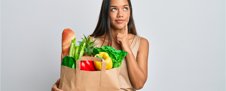 woman with shopping bag full of healthy food looks to be thinking