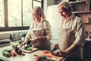 senior couple in aprons smiling while cooking together