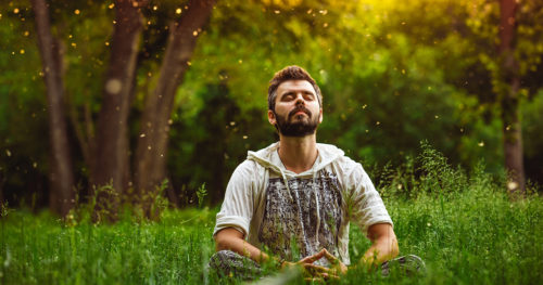Man practicing progressive muscle relaxation sitting in a field with eyes closed
