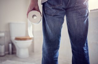 Man standing in bathroom with toilet paper