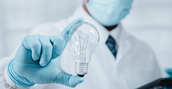 Doctor in surgical mask holds light bulb in foreground with blue gloved hand