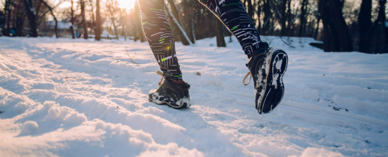 Sun shines in the background of a wooded area as a runner runs through the snow in the foreground