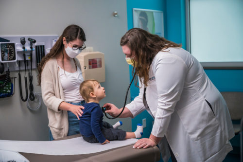 A woman and child visit an OnCall Urgent Care provider. The provider is checking the child's heart with a stethoscope.