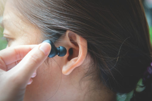 A close up woman with dark hair putting an earbud into her ear.