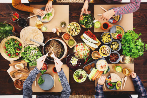 People gathered at a table of vegan, plant-based foods for a meal.