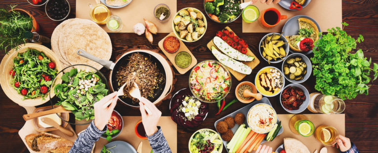 People gathered at a table of vegan, plant-based foods for a meal.