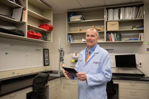 Christopher Zallek, MD, stands in the NeuroHealth Lab with a clipboard