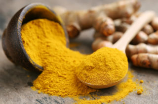 Bowl of spilled turmeric with wooden spoon full of turmeric next to it.