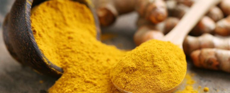 Bowl of spilled turmeric with wooden spoon full of turmeric next to it.