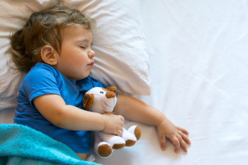 Young boy sleeping with stuffed animal.