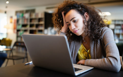 Woman with ADHD looks at her laptop with a pensive expression.