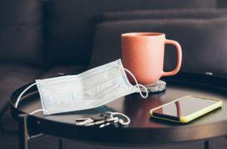 A mask sits on a coffee table next to keys and a cell phone, which brings up the question, is COVID-19 over?
