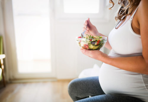 A pregnant woman eats a salad while learning about what to eat during pregnancy.