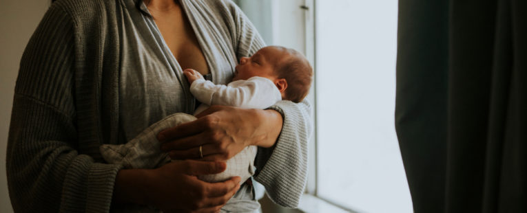 A woman holds her baby, who is not smiling, possibly due to postpartum symptoms.