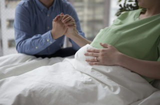 woman in hospital bed with husband, possible preterm labor, holding hands