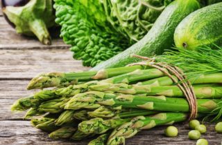 savor the season, spring into fresh produce, asparagus and green, leafy vegetables on a wooden table.