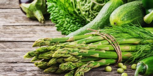 savor the season, spring into fresh produce, asparagus and green, leafy vegetables on a wooden table.