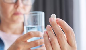 woman holding menopause supplements and a glass of water in her hand.