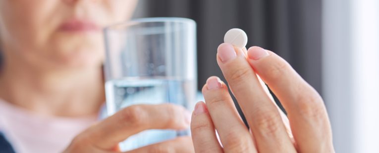 woman holding menopause supplements and a glass of water in her hand.