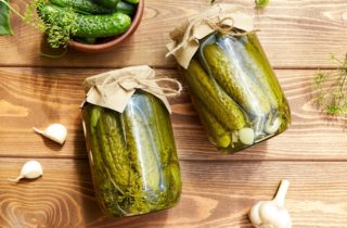 Pickled cucumbers in jars, fresh cucumbers on bowl, dill, garlic on a wooden background. Home canning. Top view.