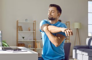 young bearded man stretches his arm across his chest sitting at his desk