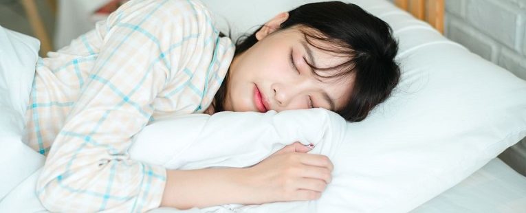 young woman sleeps on a white pillow with a blanket