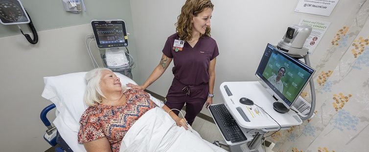 female provider in a room and a digital provider on a monitor providers care for a female patient in a hospital bed