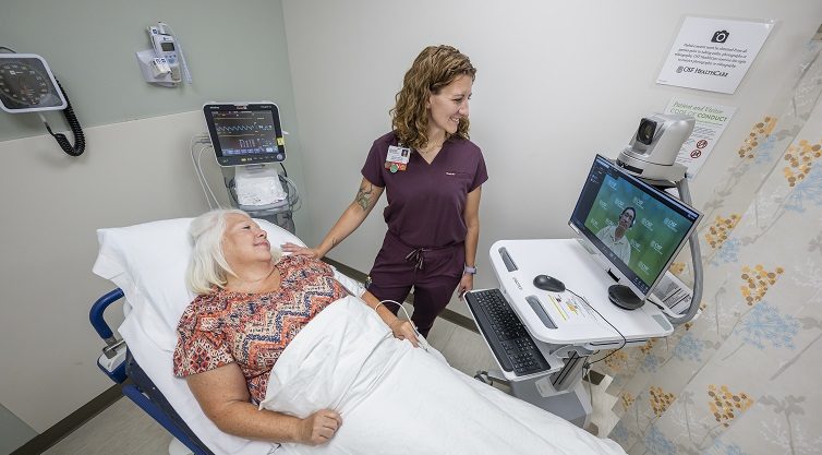 female provider in a room and a digital provider on a monitor providers care for a female patient in a hospital bed