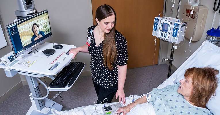female provider in a room and a digital provider on a monitor providers care for a female patient in a hospital bed