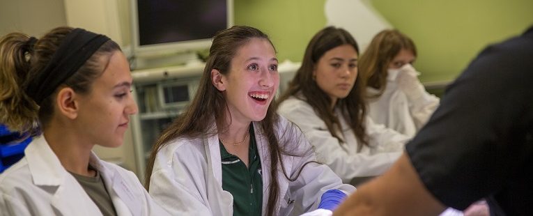 high school students in medical lab coats smile in a lab