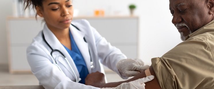 young female provider places a bandage over a male patients arm after a vaccine