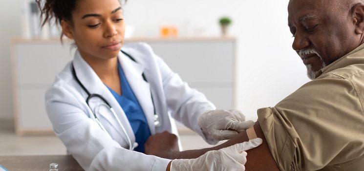 young female provider places a bandage over a male patients arm after a vaccine