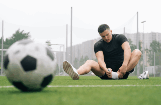 man sits and holds his ankle in front of a soccer ball