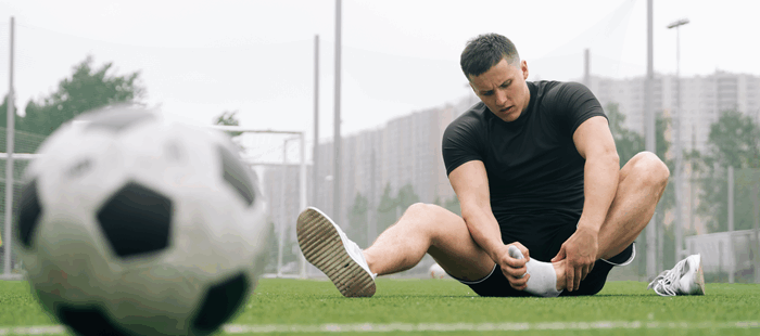 man sits and holds his ankle in front of a soccer ball